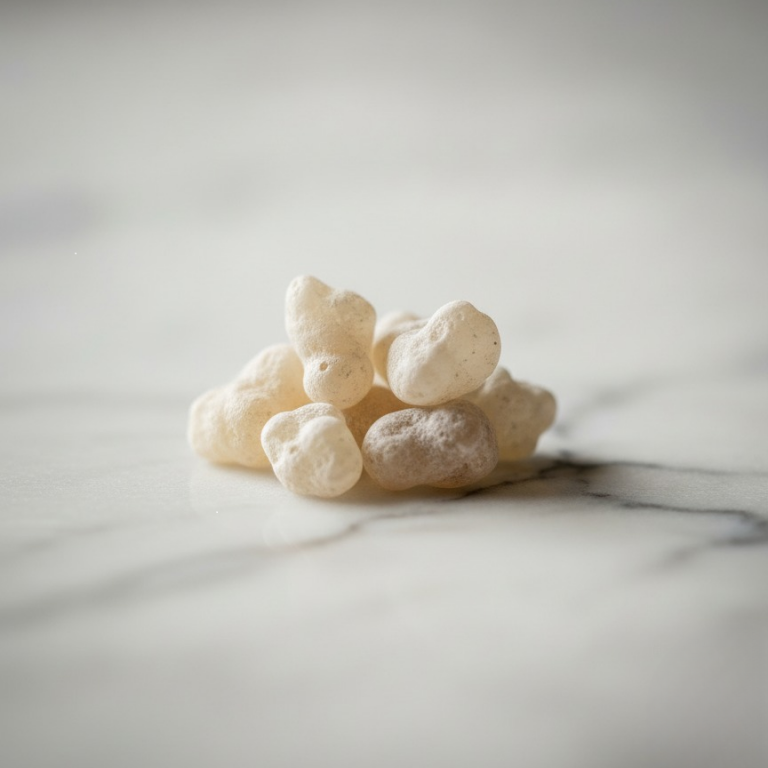 Gros plan d'une pile de larmes d'Oliban Hojari blanc pur sur une surface en marbre clair, mettant en valeur leur texture naturelle et leur translucidité.